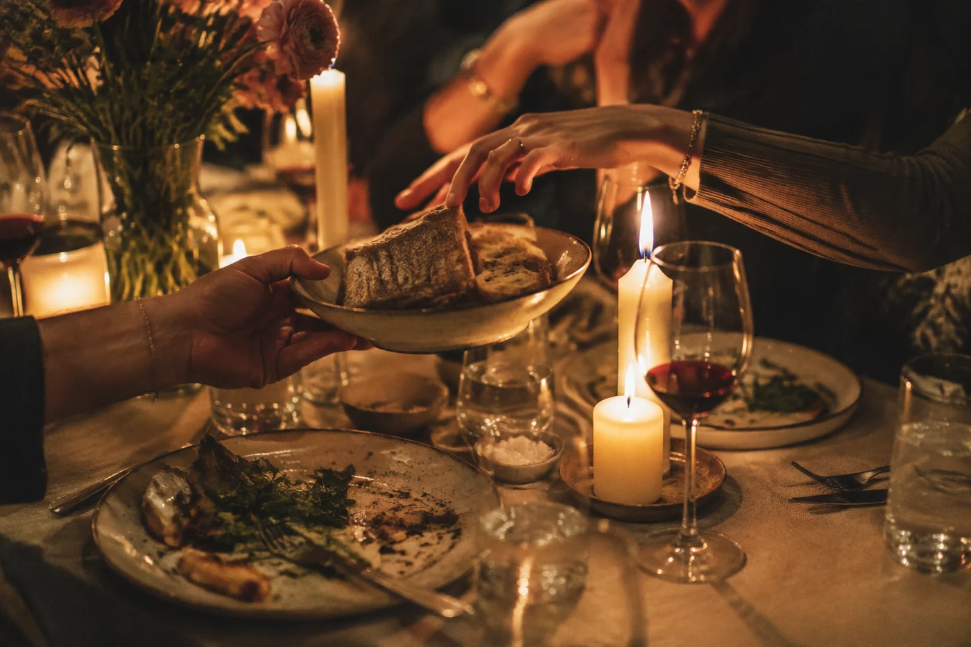 Hands passing bread across a candlelit dinner table.